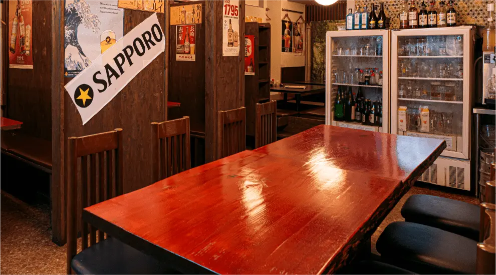 木の仕切りがあるテーブル席と、ポスターが貼られた居酒屋の店内風景。